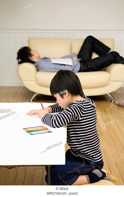 Boy drawing picture in front of father lying on sofa