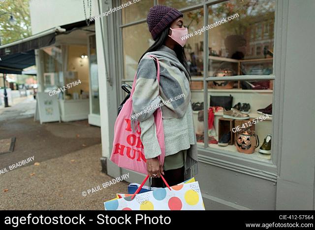 Mujer joven en mascarilla con bolsas de compras en el escaparate