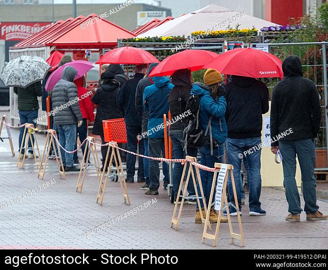 21 March 2020, Baden-Wuerttemberg, Ulm: People stand in a queue in front of a hardware store. Due to the exit restrictions in neighbouring Bavaria
