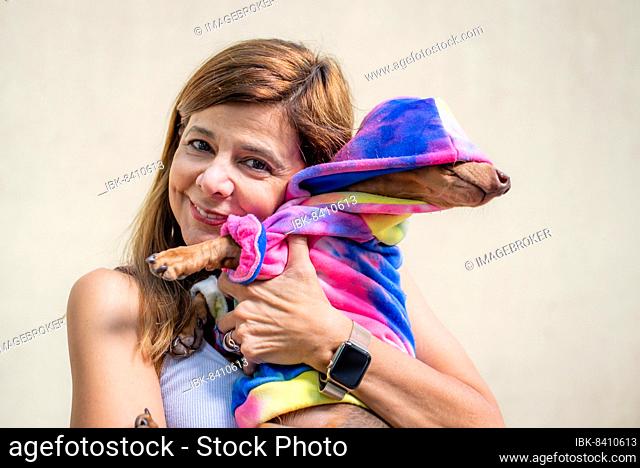 Latin woman holding her dog both dressed alike. She is looking at camera