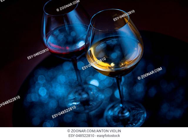 Two wineglasses on dark reflective surface with defocused lights