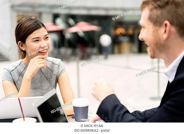 Young businesswoman and man having discussion at sidewalk cafe