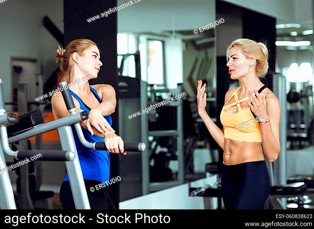 Two athletic blond women talking in the gym. Girl communicates with the trainer