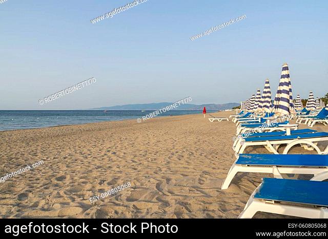 Blue and white umbrella and beach chairs at the beach in front of blue sea and blue sky. Calabria, Simeri Mare, Italy