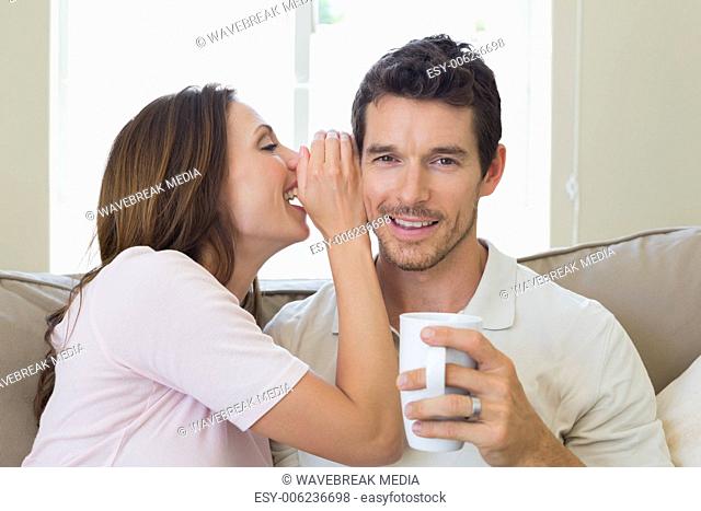 Woman whispering secret into a happy mans ear in living room