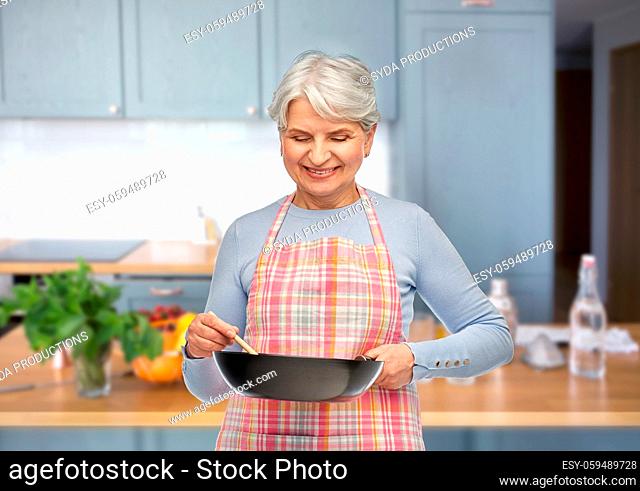 smiling senior woman in apron with frying pan
