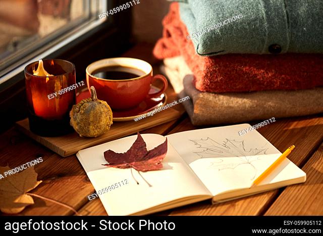 sketchbook, autumn leaf and coffee on window sill