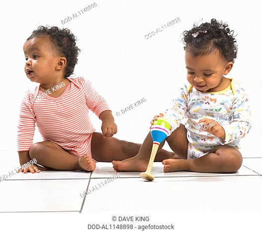 Twin boy and girl (18 months) sitting on floor, one holding a maraca