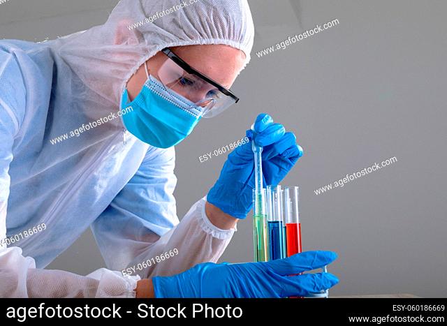Caucasian female doctor wearing ppe suit holding test-tubes