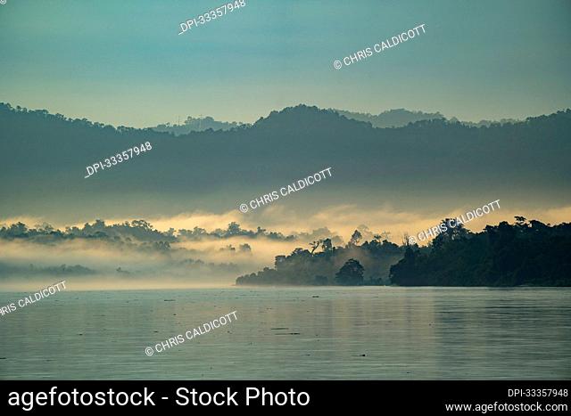 Dawn, with sunlit morning mist rising over the jungle covered banks of the Ayeyarwady (Irrawaddy) River at dawn; Rural Jungle, Kachin, Myanmar (Burma)
