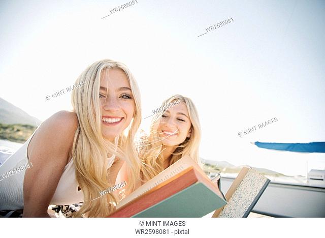 Two blond sisters lying on a jetty, reading a book