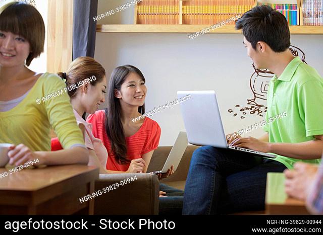 Three friends sitting in coffee shop, using laptop and talking