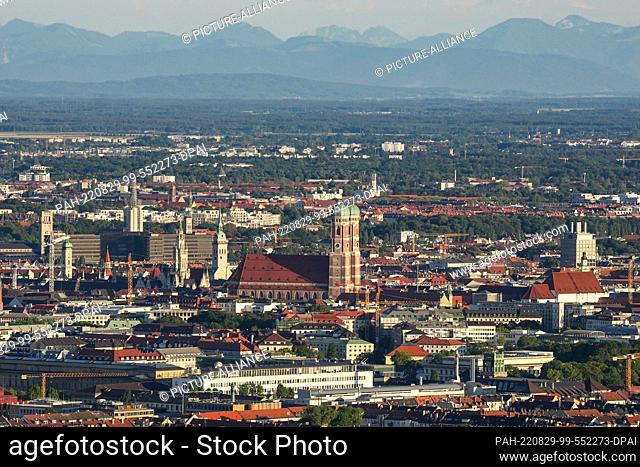 10 August 2022, Bavaria, Munich: View from the Olympiaberg to the Munich city center with the Frauenkirche. In the background you can see the mountains of the...