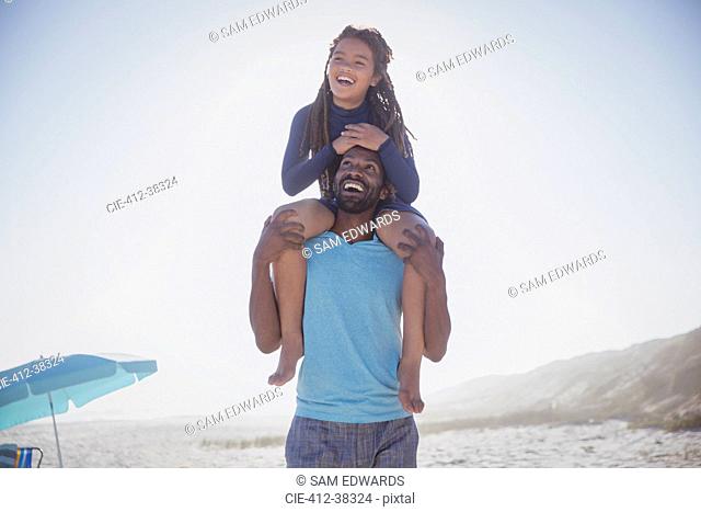 Playful father carrying daughter on shoulders on sunny summer beach