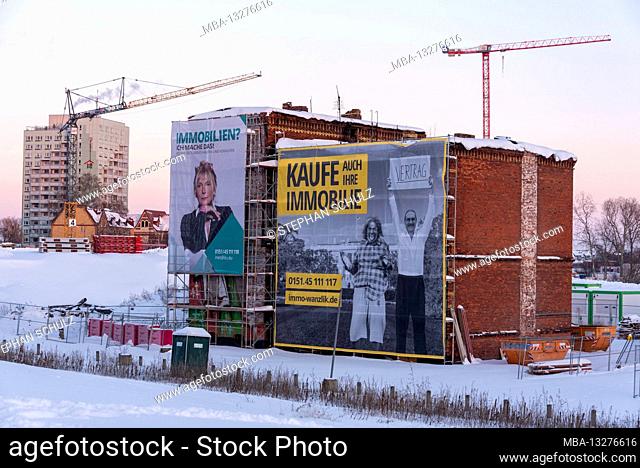 Germany, Saxony-Anhalt, Magdeburg, advertising for real estate purchases at a demolition house. Behind it are construction cranes and a high-rise
