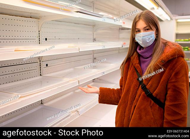 Young woman in medical face mask and empty shelves in supermarket