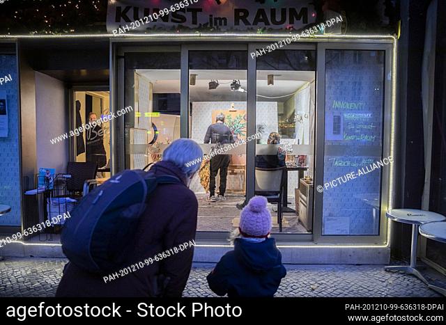 08 December 2020, Berlin: A woman and a child watch the painter Innokenti Baranov at work in a room of the café and exhibition venue Berio in Berlin-Schöneberg