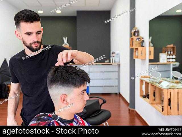 Male barber combing hair of customer while doing hairstyle at salon