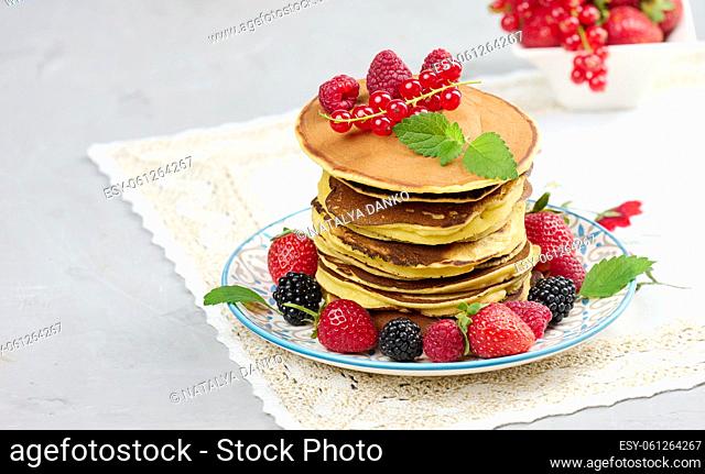 Stack of baked pancakes with fruits in a round plate on a white table