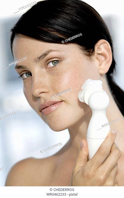 Portrait of a young woman using a massager on her face
