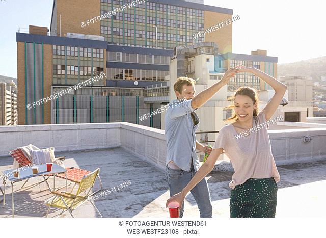 Young couple celebrating on a rooftop terrace, dancing together