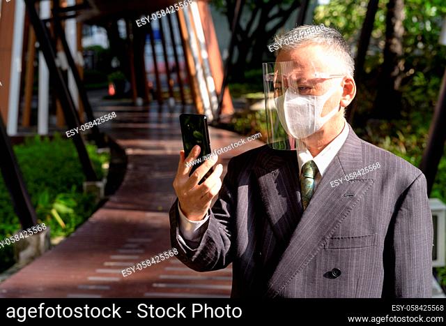 Portrait of mature Japanese businessman with mask and face shield for protection from corona virus outbreak outdoors