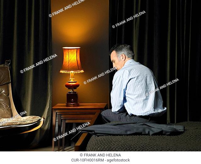 Man sitting on bed with back to camera, looking disappointed