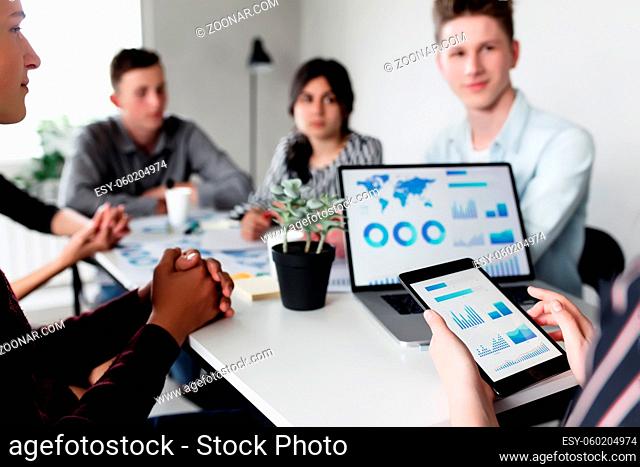 Business planning meeting, young colleagues or partners sitting together at table in conference room with graphics, charts presented by manager, discussing