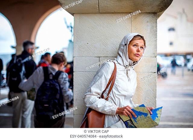 Gorgeous female tourist with a map discovering a foreign city - waiting for the rain to stop (shallow DOF; color toned image)