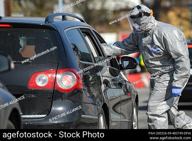 26 March 2020, Poland, Slubice: A man in a protective suit checks the body temperature of a passer-by in a car with a thermometer on the city bridge