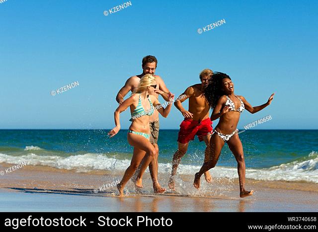 Four friends - men and women - on the beach having lots of fun in their vacation running through the water