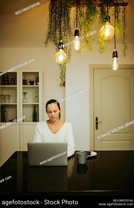 Woman using laptop by chocolate brownie and coffee at illuminated kitchen island