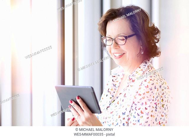 Smiling senior businesswoman holding tablet at the window
