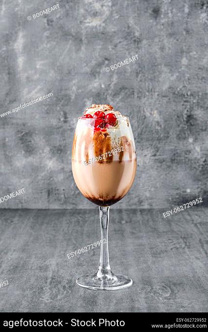 Glass of cold coffee drink with whipped cream and cherry in shabby gray background