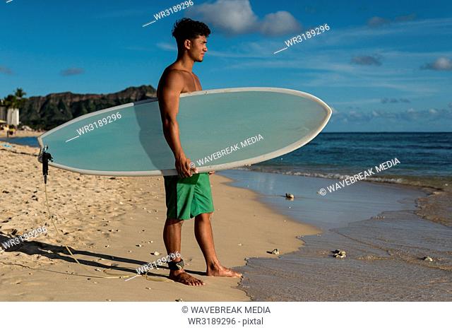 Male surfer standing with surfboard in the beach