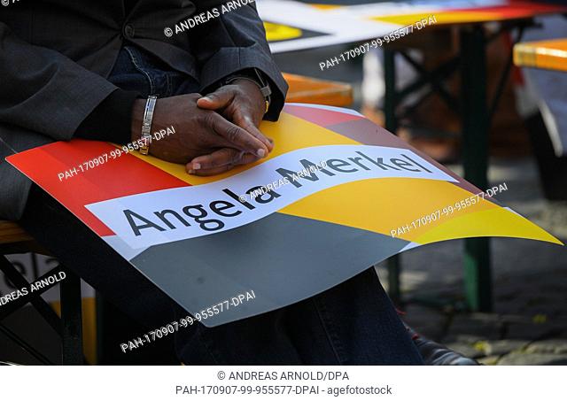A man with dark skin colour folds his hands over a poster with the name of Angela Merkel at a campaign event of the CDU party in Mainz, Germany