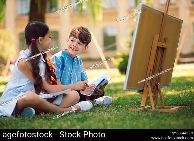 Cute Children Sitting On Grass And Making Tasks. Talking To Each Other. Education In Nature Concept
