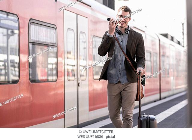 Happy young man with cell phone walking on station platform along commuter train
