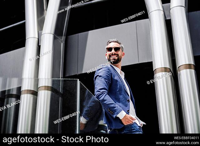 Male entrepreneur with sunglasses leaning on railing during sunny day