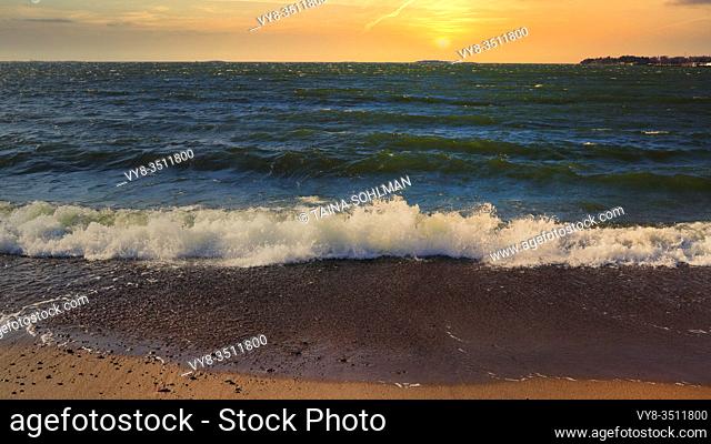 View to the sea at sunset time on a hazy evening with waves crashing on the sandy beach