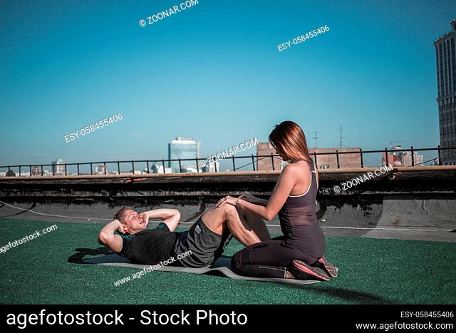 Young woman helping man with situps. Athletic man working out on abs with the help of ypung woman, outdoors sport concept