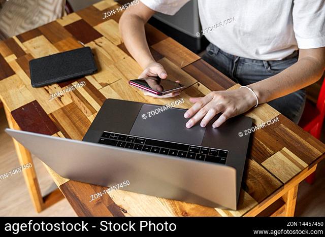 Woman's hands use a smartphone with a laptop. Study and work online, freelance. Self employed or freelance woman, girl working with her laptop sitting at wooden...