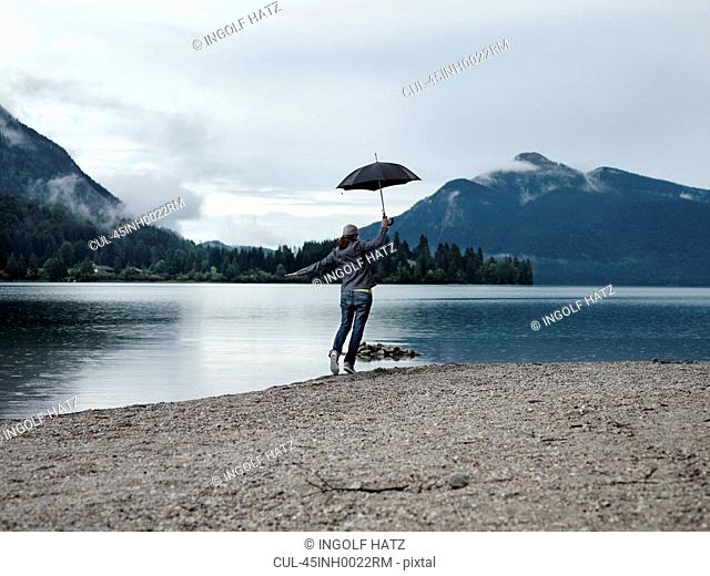 Woman carrying umbrella by still lake