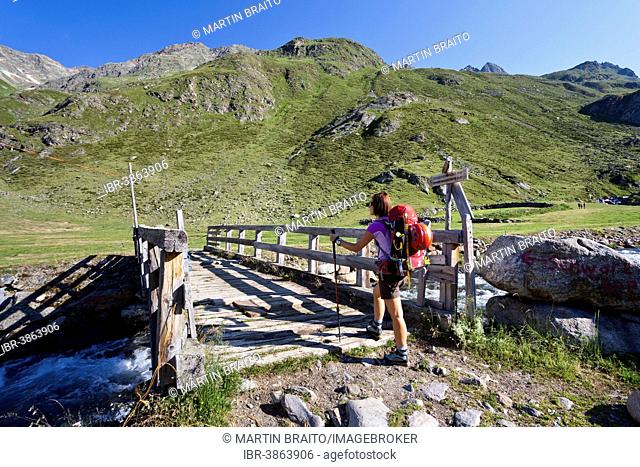 Female mountain climber at Timmelsalm alpine pasture crossing Timmlserbach stream, during the ascent to Müller Hut through the Passeiertal valley along the...