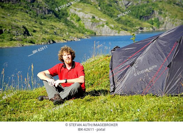 MR Young man sits at his tent in the wilderness of Moskenesoya with Agvatnet Lofoten Norway