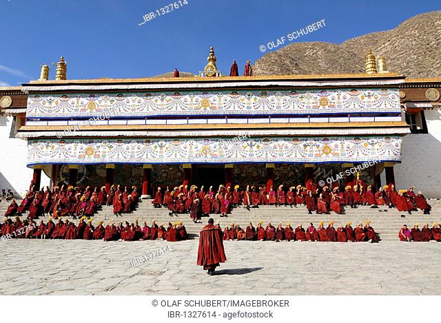 Tibetan monks wearing robes of the Gelug Order sitting on the stairs in front of the Assembly Hall, Tibetan Dukhang, the Labrang Monastery, Xiahe, Gansu, China