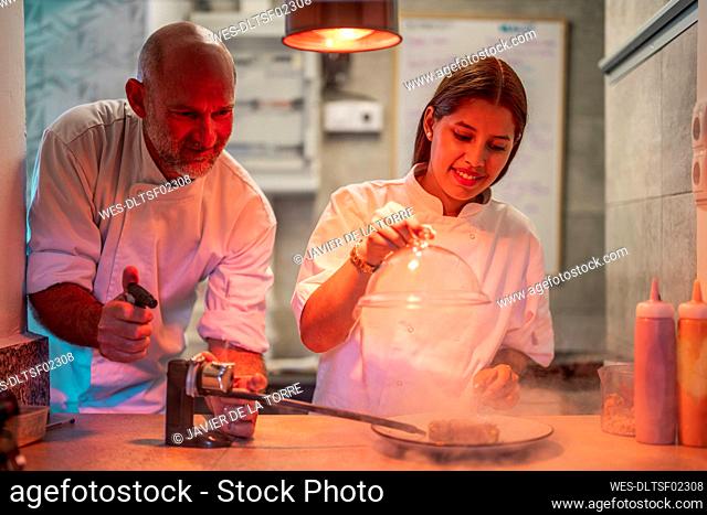 Male and female chefs smoking food in kitchen