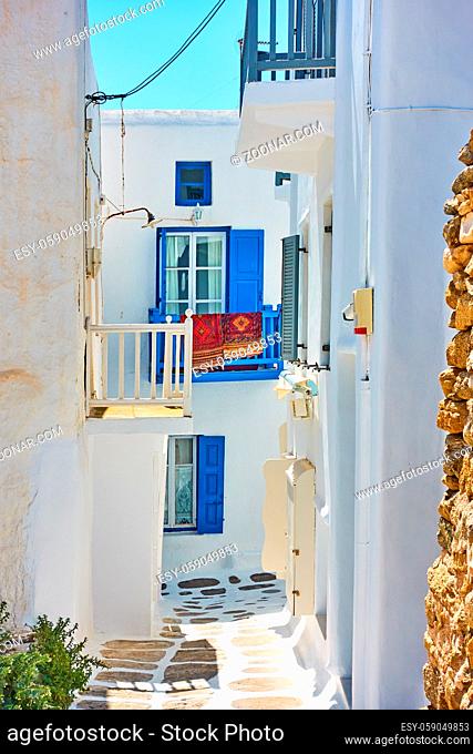 Narrow street with white small houses with balconies in Mykonos, Greece. Greek cityscape