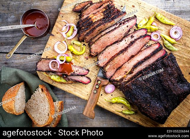 Traditional smoked barbecue wagyu beef brisket offered with farmhouse bread as top view on an old cutting board with Louisiana sauce, onion rings and peperoni