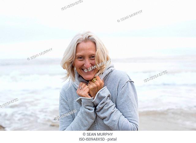 Mature woman wearing grey sweater on beach, smiling